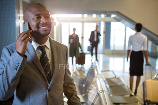 Бизнесмен разговаривает по мобильному телефону в зоне ожидания в терминале аэропорта — стоковое фото