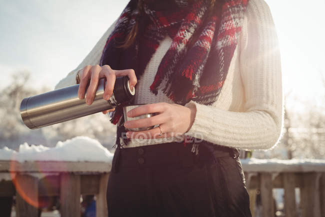 Mid section of woman in winter wear pouring drink in cup during ski holidays — Stock Photo