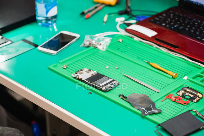 Piezas de teléfono móvil desmontadas en una mesa en un centro de reparación - foto de stock
