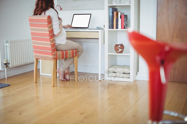 Mujer embarazada usando el ordenador portátil en la sala de estudio en casa - foto de stock
