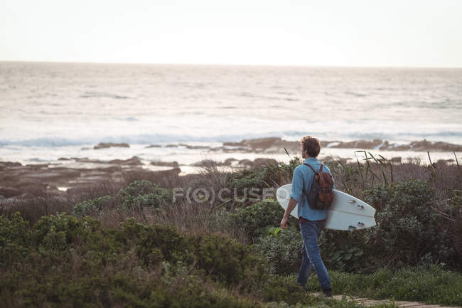 Чоловік, що несе дошку для серфінгу, що йде до моря — стокове фото