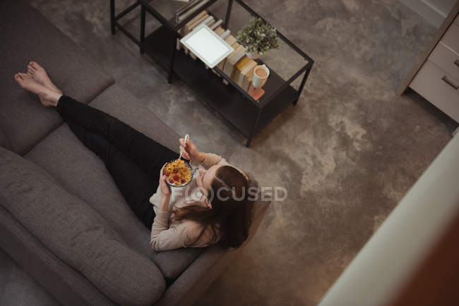 Donna seduta sul divano e avendo ciotola di ciotola di cereali una casa — Foto stock
