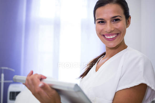 Портрет улыбающегося стоматолога с помощью цифрового планшета в клинике — стоковое фото