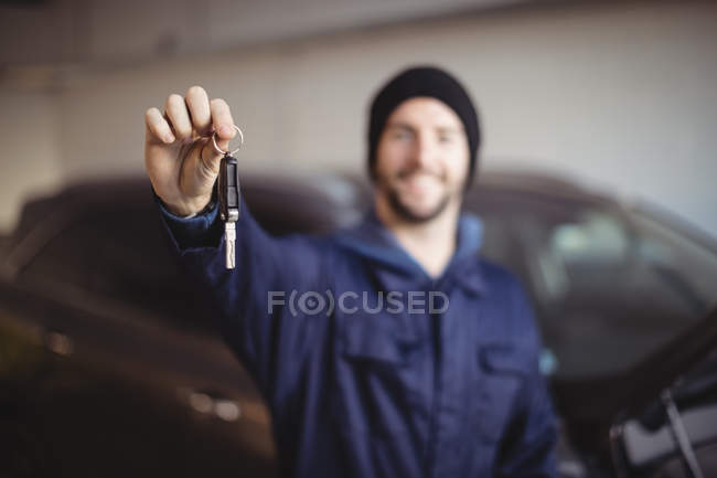 Mecánico sonriente en garaje sosteniendo la llave del coche - foto de stock