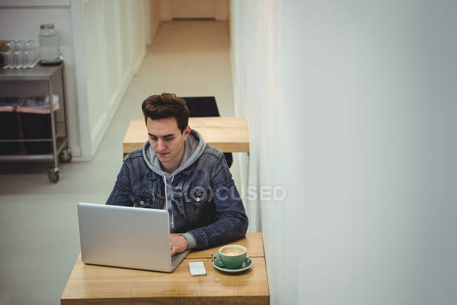 Homem usando laptop com xícara de café na mesa no café — Fotografia de Stock