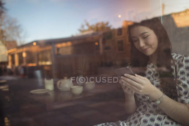 Donna che utilizza il telefono cellulare vicino alla finestra al caffè — Foto stock