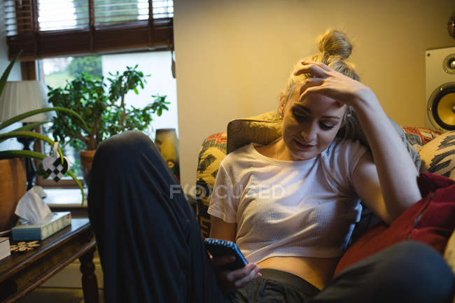 Donna sdraiata e utilizzando il telefono cellulare sul divano in soggiorno a casa — Foto stock