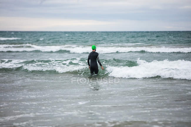 Вид ззаду спортсмена в мокрій костюмі, що йде в бік моря — стокове фото