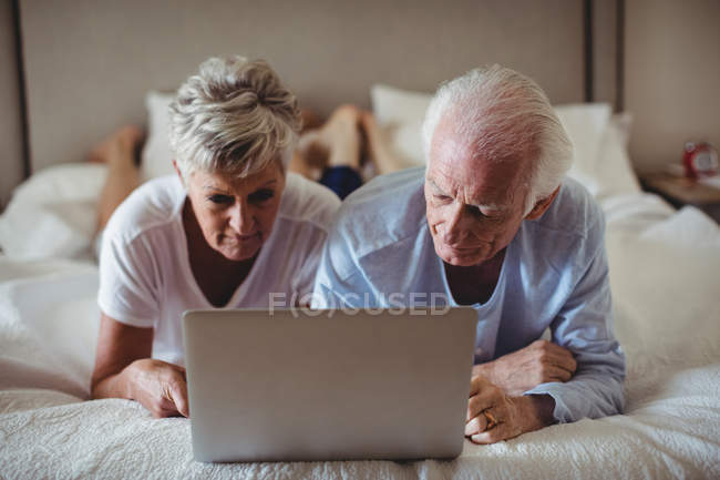Senior couple lying on bed and using laptop in bed room — Stock Photo
