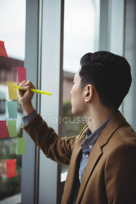 Ejecutivo de negocios escribiendo en notas adhesivas en la oficina - foto de stock