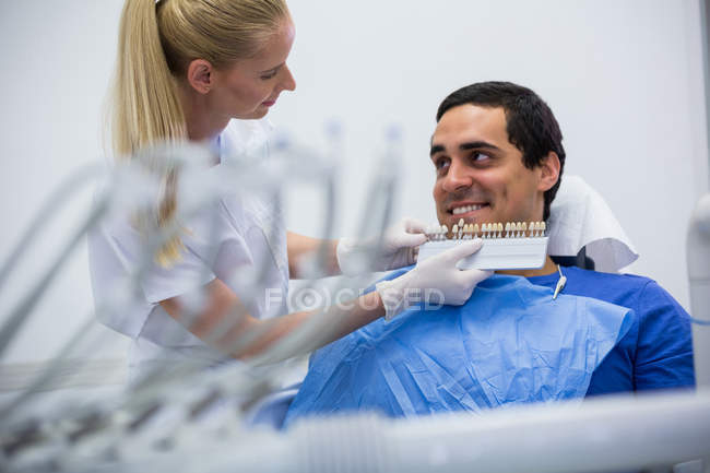 Dentist examining female patient with teeth shades at clinic — Stock Photo