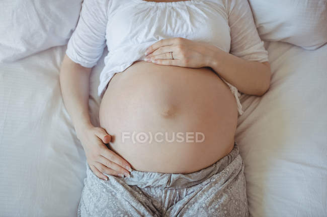 Partie médiane de la femme enceinte se détendre sur le lit dans la chambre — Photo de stock