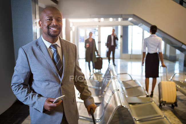 Portrait of businessman with phone and trolley bag standing at airport terminal — Stock Photo