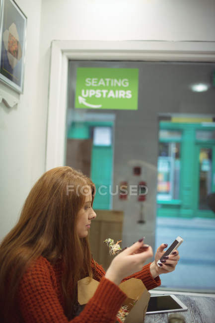 Femme rousse utilisant un téléphone portable tout en mangeant de la salade — Photo de stock