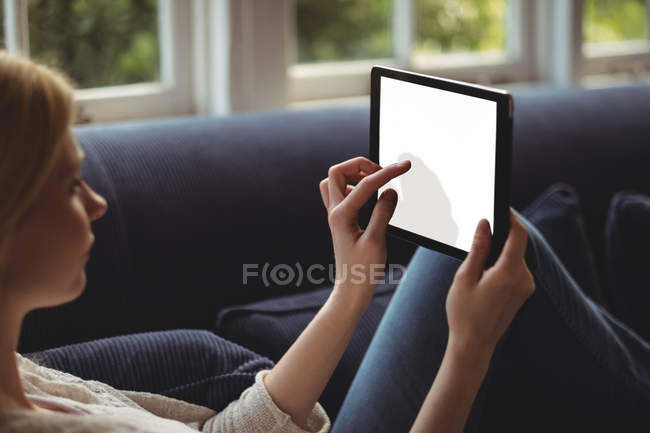 Woman sitting on sofa with digital table in living room at home — Stock Photo