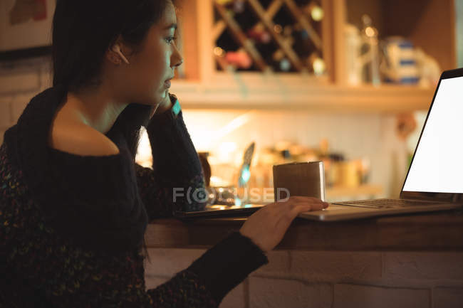 Femme utilisant un ordinateur portable sur le comptoir de la cuisine à la maison — Photo de stock