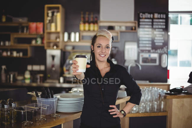 Retrato de camarera de pie con taza de café desechable en la cafetería - foto de stock