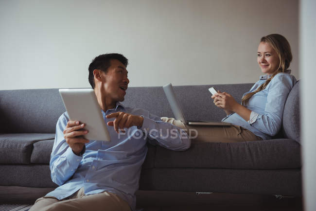 Casal usando telefone celular, laptop e tablet digital em casa — Fotografia de Stock