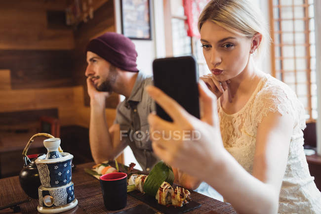 Woman taking selfie while man talking on phone in restaurant — Stock Photo