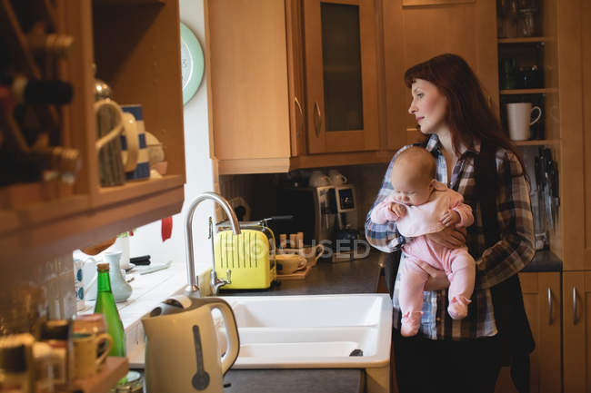Madre sosteniendo pequeño bebé en la cocina en casa - foto de stock