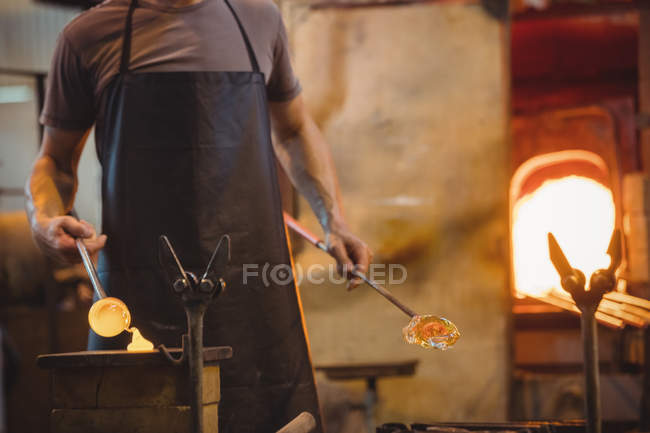 Mid section of glassblower shaping a molten glass at glassblowing factory — Stock Photo
