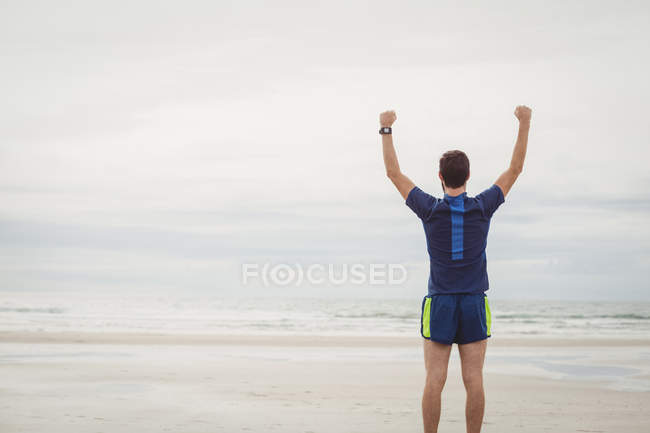 Visão traseira do atleta em pé na praia com as mãos levantadas — Fotografia de Stock