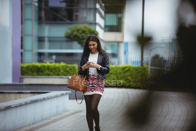 Щаслива жінка використовує мобільний телефон під час ходьби в офісних приміщеннях — стокове фото