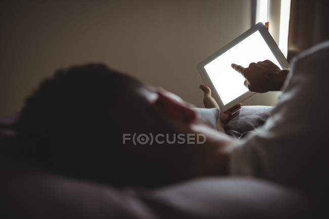 Вид ззаду людини, використовуючи свій цифровий планшет, розслабляючись на ліжку в спальні — стокове фото