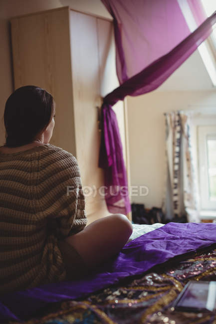 Frau sitzt zu Hause auf Bett im Schlafzimmer — Stockfoto