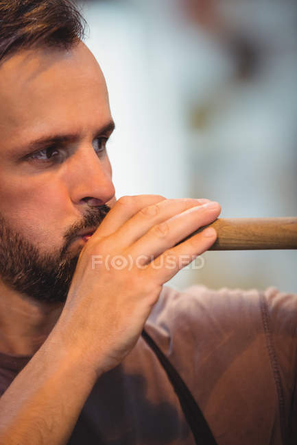 Close-up of glassblower blowing a blowpipe at glassblowing factory — Stock Photo