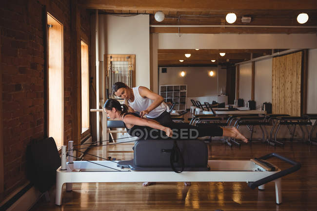 Инструктор, помогающий женщине во время занятий пилатесом в фитнес-студии — стоковое фото