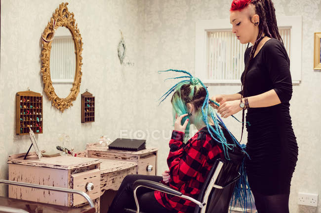 Beautician style clients hair in dreadlocks shop — стоковое фото