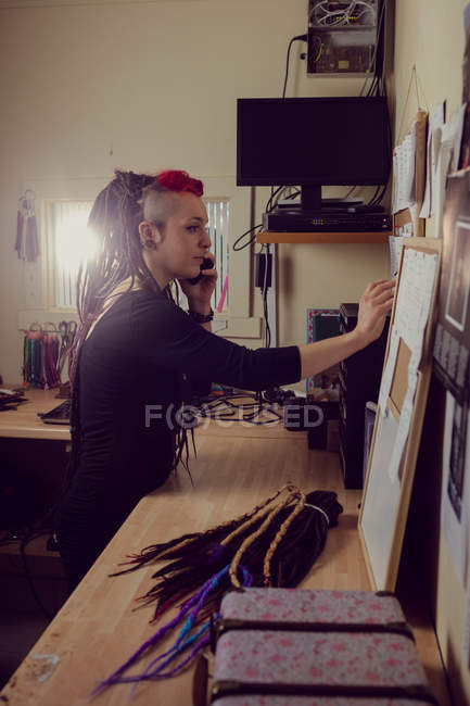 Female hairdresser talking on mobile phone and making notes in dreadlocks shop — Stock Photo