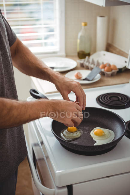 Mid-section of man cracking an egg into a frying pan in the kitchen at home — Stock Photo