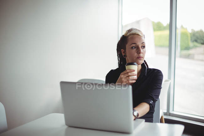 Mujer tomando café mientras usa el ordenador portátil en la cafetería - foto de stock