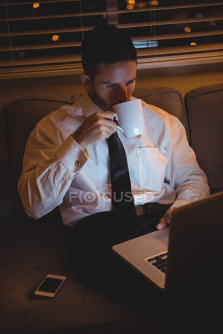 Empresário usando laptop enquanto toma café em casa — Fotografia de Stock