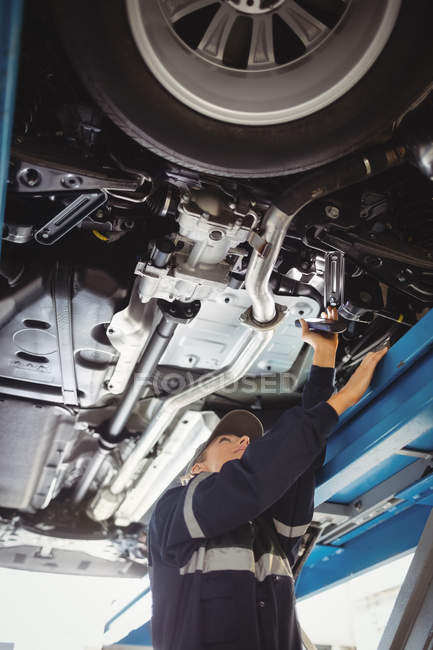 Mechanikerin untersucht Auto mit Taschenlampe in Werkstatt — Stockfoto