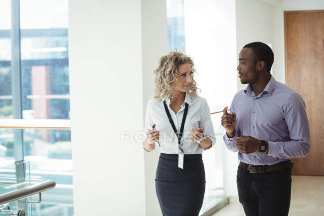 Female and male business executives having a discussion while walking in corridor at office — Stock Photo