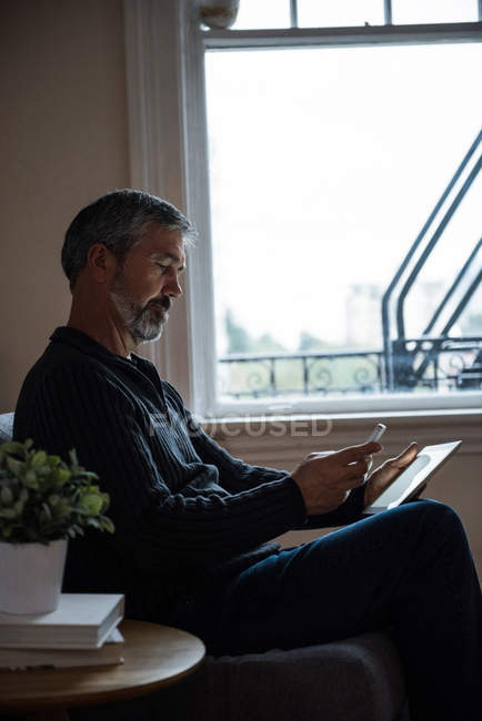Man using mobile phone and digital tablet in living room at home — Stock Photo