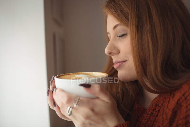 Primer plano de la hermosa mujer sosteniendo la taza de café en la ventana - foto de stock