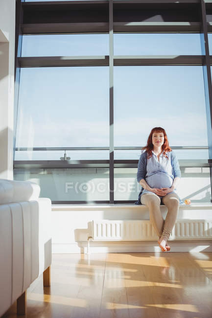 Femme enceinte assise près de la fenêtre dans le salon à la maison — Photo de stock