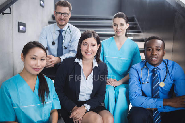 Retrato de doctores y enfermeras sonrientes sentados en la escalera del hospital - foto de stock
