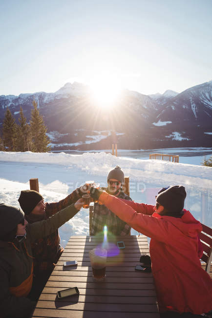 Gli amici sciatori brindano bicchieri di birra nella stazione sciistica durante l'inverno — Foto stock