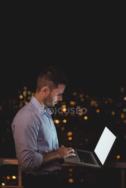 Homem usando laptop na varanda à noite — Fotografia de Stock