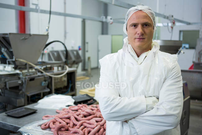 Porträt eines männlichen Metzgers, der mit verschränkten Armen in einer Fleischfabrik steht — Stockfoto