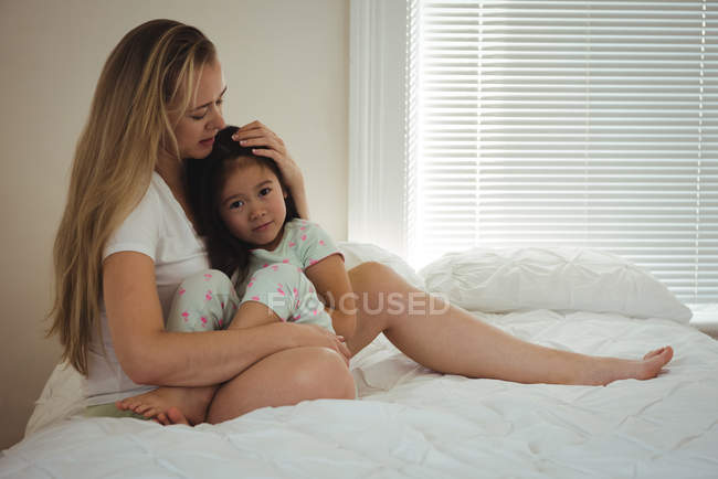 Любящая мать обнимает дочь в спальне дома — стоковое фото