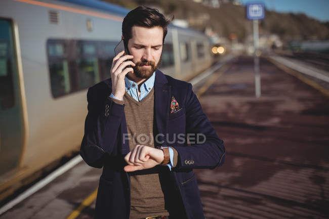 Бізнесмен перевіряє час під час розмови на мобільному телефоні на залізничній станції — стокове фото