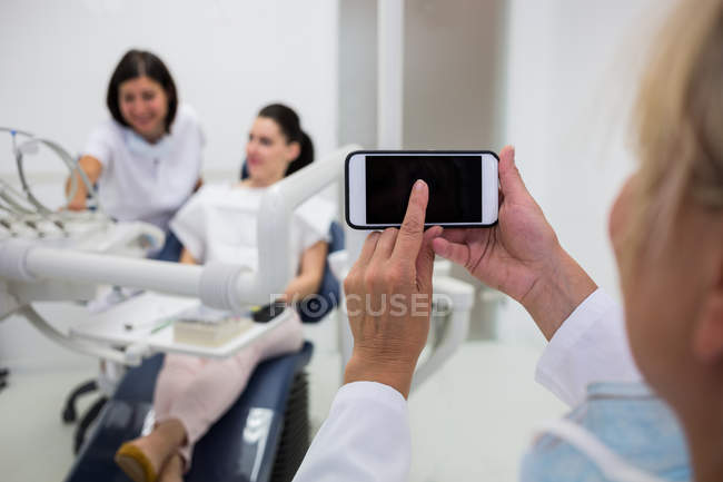 Frau benutzt Handy in Klinik mit Menschen im Hintergrund — Stockfoto