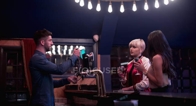 Barman interagindo com mulheres bonitas no balcão no bar — Fotografia de Stock