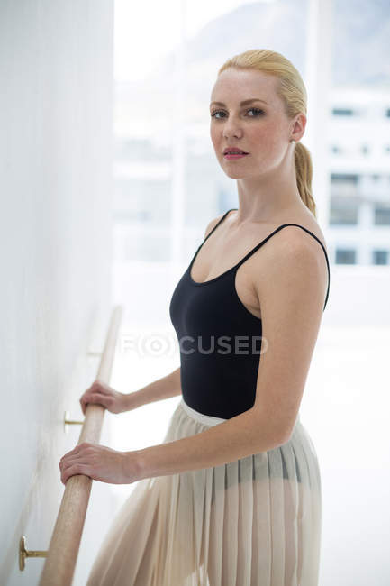 Bailarina estirándose en una barra mientras practica ballet en el estudio - foto de stock